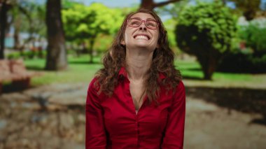Kırmızı gömlekli kadın, güneşli bir günde yemyeşil yemyeşil parklarla çevrili açık havada mutluluk ve sükunet içinde gülümsüyor..