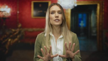 Genç bir kadın, kırmızı duvarları, zarif dekorları ve sükuneti olan lüks bir müzede sakince el kol hareketleri yapıyor..