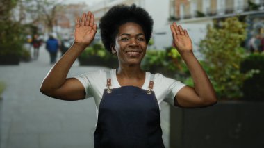 Yoğun şehir caddesinde önlükle gülümseyen bir kadın, doğal arka planda şehir manzarasını yakalıyor, canlı şehir yaşamını ve farklı metropol ortamlarını aktarıyor..