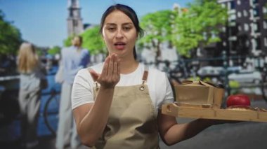 Elinde ahşap bir tepsi taşıyan ve Amsterdam 'da sokakta öpücük yollayan bej rengi önlük giyen bir kadın misafirperverliği hoş karşılıyor..
