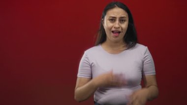 Elleri ağzı kaplayan ve kırmızı stüdyo ortamında avuçları görünen bir kadın, korkmuş endişeli bir ifade, şok sessizliği..