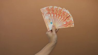 Kafkasyalı bir adamın eli, kahverengi duvar arkasında birden fazla Filipinli peso tutuyor..