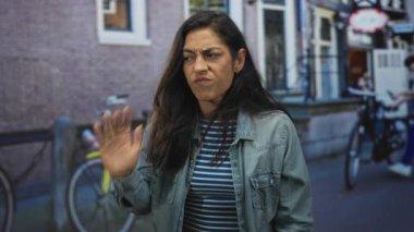 Sarı bisiklet ve tuğla bir binanın yanında somurturken kot ceketli kadın el pençe divan duruyor..