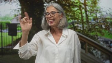 Kadın ağaçların altında el sallarken ve parmaklıklar arasında bardakları ayarlarken; dostça selamlaşma bağlantısı.