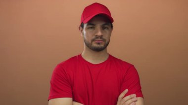 Kırmızı şapkalı ve tişörtlü genç İspanyol teslimatçı şeftali stüdyosu ortamında kollarını kavuşturuyor..