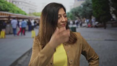 Kahverengi ceket giyen İspanyol kadın, sokak pazarındaki ahşap hediyelik eşya dükkanını işaret ediyor..