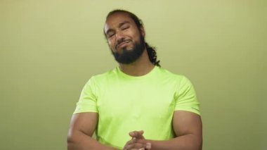 Stüdyoda yeşil duvara karşı el çırpan adam, neon yeşil gömlek ve sakal giyiyor görünür; onay teşvik.