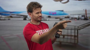 Cankurtaran kırmızı tişört giyen ve elinde dürbün tutan havalimanı pistini işaret eden gülümseyen adam, tetikte olma görevi.