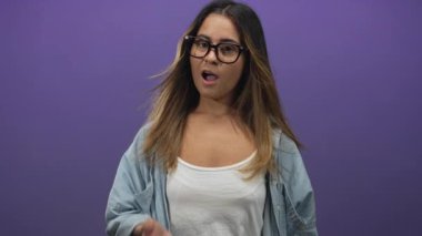 Göğsünde gözlük, beyaz atlet ve kot gömlek giyen, mor stüdyoda uzun saçlı ve sarı tırnaklı bir kadın; sürpriz hassasiyet.