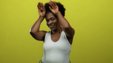 Neşeli bir şekilde gülümseyen ve el kaldıran bir kadın neşeli bir tavırla, neşeli bir ifadeyle parlak sarı arka plana karşı, neşe ve pozitiflik taşıyan bir kadın..