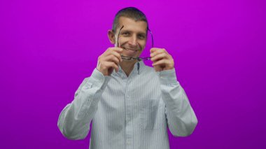 Beyaz adam gülümserken parlak pembe arka planda gözlük çıkartıyor, çizgili bir tişört giyiyor ve neşeli bir ifade takınıyor, tefekkür ve mizah anı yakalıyor..