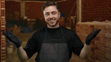 İnşaat alanında gülümseyen önlük ve eldiven takan sakallı genç adam, kapalı servis ya da devam eden bir iş öneriyor..