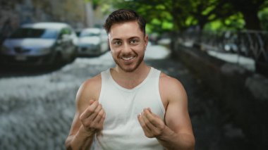 Sakallı genç adam yazın gülümseyen beyaz kolsuz tişörtlü şehir sokaklarında para dağıtıyor..