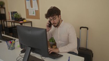 Ofisteki genç adam akıllı telefonuyla konuşuyor. İş iletişimine odaklanıyor. Etrafı tahta, masa ve profesyonel bir çevreyi yansıtan belgelerle çevrili..