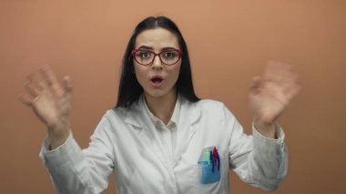 Gözlük takan bilim adamı kahverengi duvara karşı jestler yapıyor, seyircilerle irtibat kuruyor, profesyonel çevreyi ve iletişimi vurguluyor.