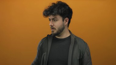 Sakallı genç İspanyol adam turuncu arka plana şaşırmış görünüyor.