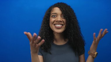 Afrikalı Amerikalı bir kadın gülümserken saçı parlak mavi bir stüdyo duvarına yaslanırken iyimserlik.