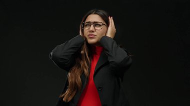 Gözlüklü genç bir kadın, izole edilmiş siyah arka plan yüzünden stresli, resmi giyinmiş, hayal kırıklığını ve kaygıyı anlamlı bir şekilde gösteriyor..