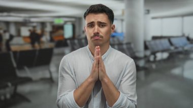 İspanyol bir adam yoğun havaalanında arka planı bulanık bir şekilde acil seyahat ve beklenti içinde yalvarıyor.