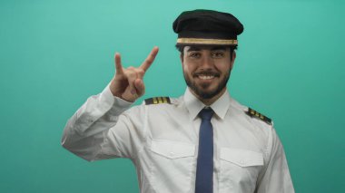 Sakallı, pilot üniforması giyen genç bir İspanyol yeşil arka plana karşı taş bir jest yapıyor, rahat ve kendinden emin bir tavır sergiliyor..