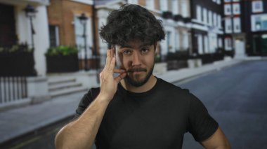 Kentsel sokak ortamında sakallı genç bir adam düşünceli ve anlamlı bir görünüm sergiliyor. İspanyol mirası ve günlük kıyafetleri gözler önüne seriyor..