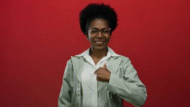 Genç Afrikalı Amerikalı kadın gülümseyen ve işaret eden kırmızı arka plan, pozitiflik ve güven taşıyor.