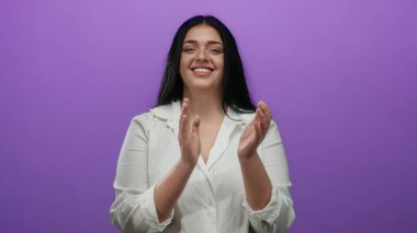 İzole edilmiş mor arka planda, beyaz gömlek giyen, kendine güveni ve pozitifliğiyle mutlu bir şekilde alkışlayan kadın..