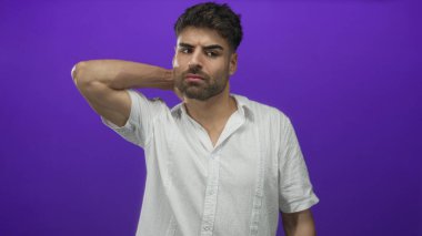 Beyaz tişörtlü, boyuna dokunan ve mor stüdyoda somurtan yumuşak ışıkla aydınlatılan Latin asıllı genç adam..