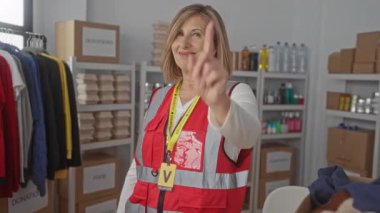 Kadın, kapalı bağış merkezindeki kamerayı işaret ediyor. Doldurulmuş kutular ve asılı giysilerle. Merhamet..