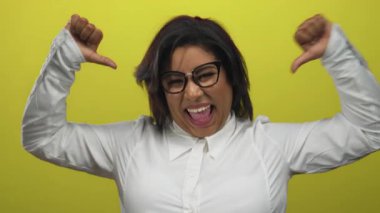 Gülümseyen, iri yarı İspanyol kadın, beyaz gömlekli, kendine güveni ve enerjisi olan, parlak sarı bir arka plana işaret ediyor..