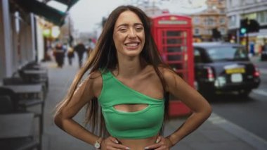 Meşgul şehir caddesinde kırmızı telefon kulübesi ve taksisiyle kamerayı gösteren bir kadın..