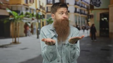 Sıradan kot ceket giyen beyaz sakallı genç adam şehir sokaklarında avuçlarını açık tutuyor..
