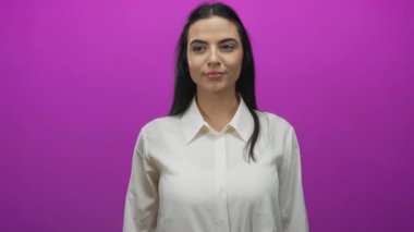 Beyaz tişörtlü genç İspanyol kadın canlı pembe duvara karşı duruyor. Çeşitli yüz ifadeleriyle şaşkınlık ve mutluluğu ifade ediyor..