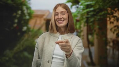 Bahçede gülümseyen genç sarışın kadın yemyeşil bir alanda neşeli bir şekilde ve sıcak, davetkar bir atmosferde bir neşe anı yakalıyor..