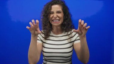 Çizgili bluz giyen kadın parlak mavi stüdyoda kükreyen el hareketleriyle yayılıyor; enerjik bir eğlence..