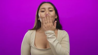 Pembe yumuşak dudaklı ve elini kaldırmış bir kadın mor stüdyoda öpücük hareketi yapıyor..