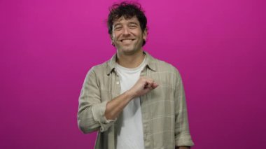 İspanyol adam gülümsüyor ve pembe arka plana doğru yumruğunu uzatıyordu. Günlük gömlek giyiyordu. Pozitif bir hareket ve kendinden emin bir ifade sergiliyordu..