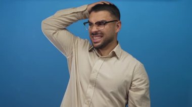 Genç İspanyol adam parlak mavi bir stüdyo duvarına gözlük ayarlar, çatık kaşlı ve gergin bir duruş ile şaşı; kafa karışıklığı.