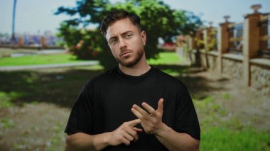 Sakallı bir adam, yeşil çimen ve ağaçlarla kaplı güneşli parkta parmaklarını sayıyor..