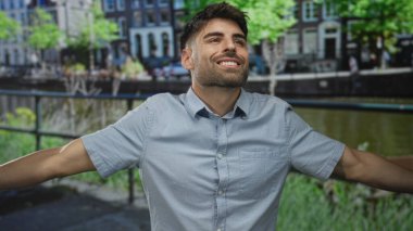 Genç Hispanik adam çıplak kollarını açar ve başını güneş ışığı sokağındaki kanal korkuluklarına yaslar; dinginlik.