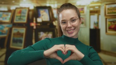 Resimlerle çevrili renkli sanat galerisinde elleri olan bir kadın kalp şekli oluşturuyor..