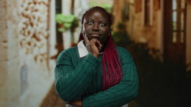 Şehir caddesinde açık havada duran bir kadın düşünceli bir ifade ve örgü örerek kentsel çevreyi gösteren binalarla çevrili bir şeyi sorguluyor.