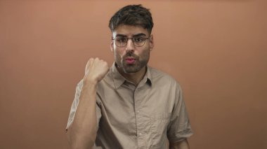 Stüdyoda şeftali duvarına karşı sıkılmış yumruğu ve büzüşmüş dudakları olan İspanyol bir adam..