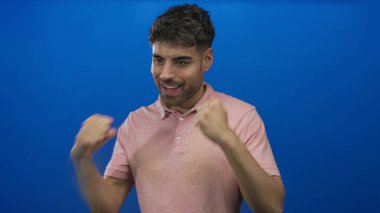 Parlak mavi bir stüdyoda yumruklarını sıkmış ve geniş bir gülümsemesi olan genç bir adam. Gurur güveni hırsı motivasyonu..