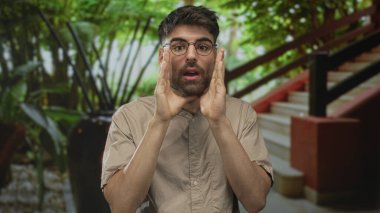 Yeşilliğe tepeden bakan bir merdivenin yanındaki modern bir binanın lobisinde elleri ağıza dolamış ve temiz bir sesle bağırıyor; acil uyarı uyarısı.