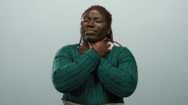 Yeşil kazaklı Afro-Amerikalı kadın, izole edilmiş beyaz arka plan karşısında boyun ağrısı çekiyor. Rahatsızlık ve gerilim gösteriyor..
