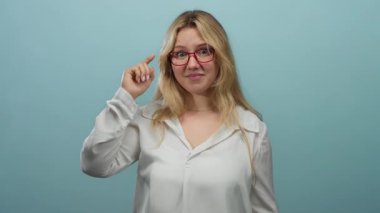 Gözlüklü genç sarışın kadın beyaz izole bir arka plan duvarından deli gibi el kol hareketi yapıyor. Kafa karışıklığı ya da delilik anlamına geliyor.