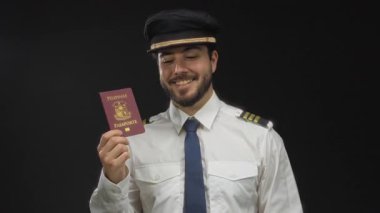 Siyah arka plan, seyahat ve profesyonel havacılık temalarına karşı Filipin pasaportu tutarken sakallı genç bir pilot gülümsüyor..