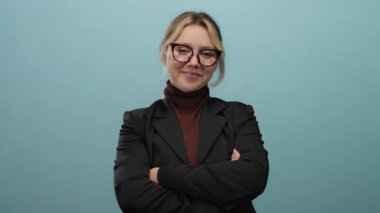 Gözlüklü, siyah ceketli ve kolları mavi bir arkaplanda uzanan bir kadın profesyonel ve yaklaşılabilir bir tavır sergiliyor..