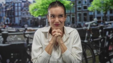 İspanyol kadın ellerini çenesinin altına katlıyor ve kanalın yanında bisikletler olan bir sokakta yoğun bir ifade sergiliyor..